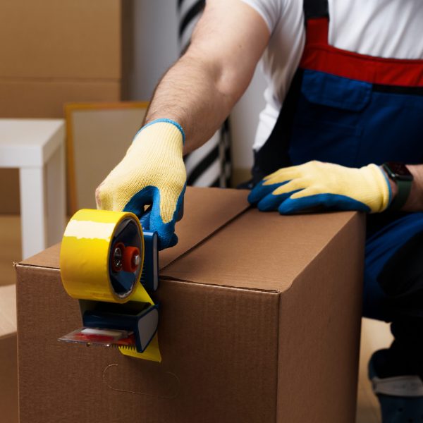 Man mover in uniform packing boxes with scotch tape, close up